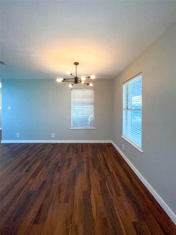 empty room featuring an inviting chandelier and dark wood-type flooring