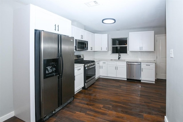 kitchen with appliances with stainless steel finishes, dark hardwood / wood-style flooring, backsplash, sink, and white cabinetry