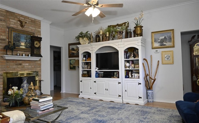 living room featuring hardwood / wood-style floors, ceiling fan, crown molding, and a brick fireplace