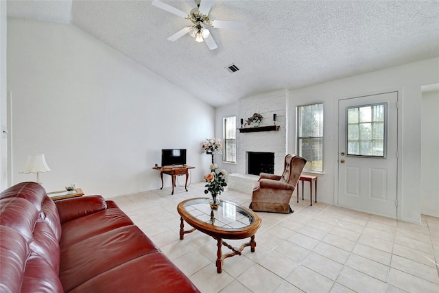 living room with a stone fireplace, ceiling fan, light tile patterned floors, and lofted ceiling