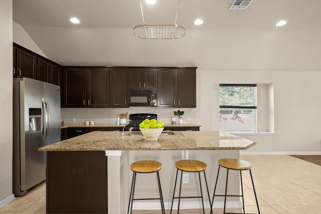 kitchen featuring black appliances, a center island with sink, light tile patterned floors, light stone counters, and a kitchen bar