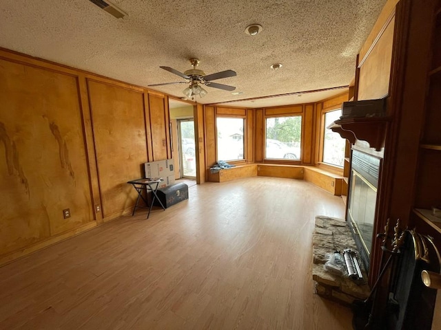 miscellaneous room with hardwood / wood-style floors, a textured ceiling, a stone fireplace, and ceiling fan