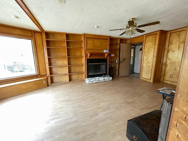 living room featuring ceiling fan, a fireplace, light hardwood / wood-style floors, and a textured ceiling