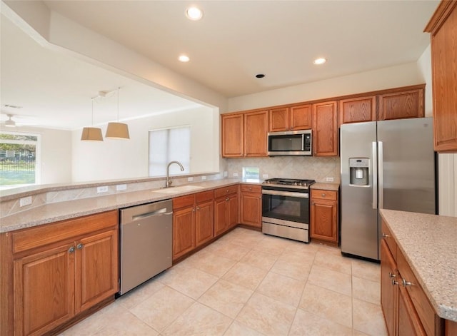 kitchen featuring kitchen peninsula, appliances with stainless steel finishes, light stone countertops, sink, and hanging light fixtures