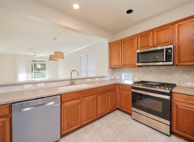 kitchen featuring sink, stainless steel appliances, tasteful backsplash, light stone counters, and decorative light fixtures