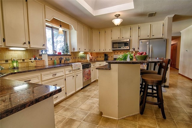 kitchen featuring a kitchen breakfast bar, tasteful backsplash, dark stone counters, stainless steel appliances, and a center island