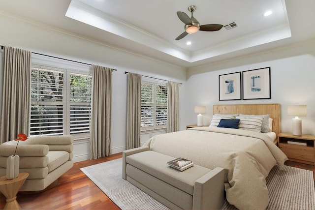 bedroom with hardwood / wood-style flooring, a tray ceiling, and multiple windows