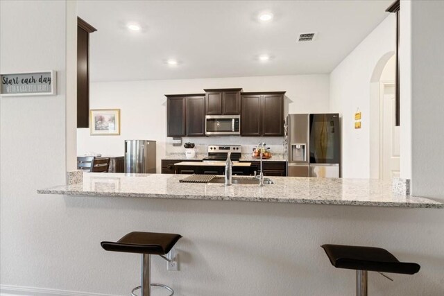 kitchen featuring appliances with stainless steel finishes, light stone counters, and kitchen peninsula