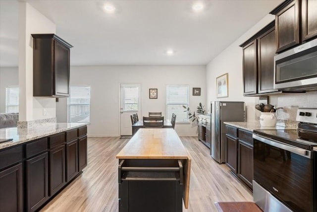 kitchen featuring dark brown cabinetry, light wood-type flooring, light stone countertops, and appliances with stainless steel finishes