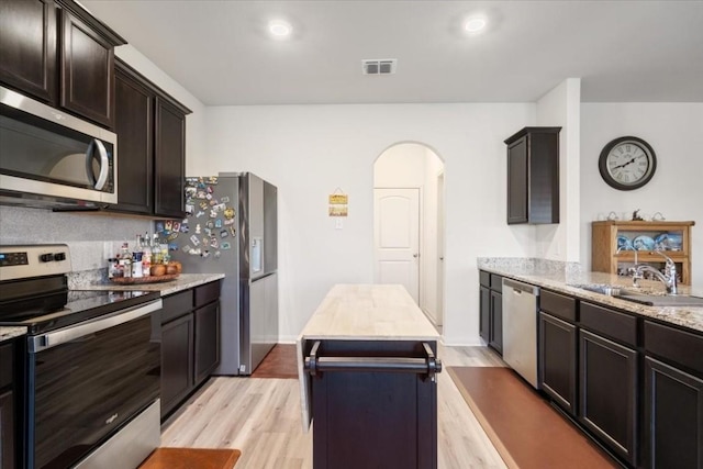 kitchen featuring sink, stainless steel appliances, light stone counters, light hardwood / wood-style floors, and a kitchen island