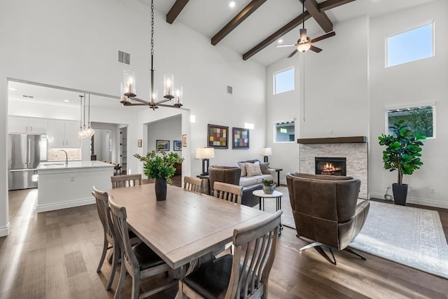 dining room featuring a stone fireplace, beamed ceiling, high vaulted ceiling, dark hardwood / wood-style floors, and ceiling fan with notable chandelier