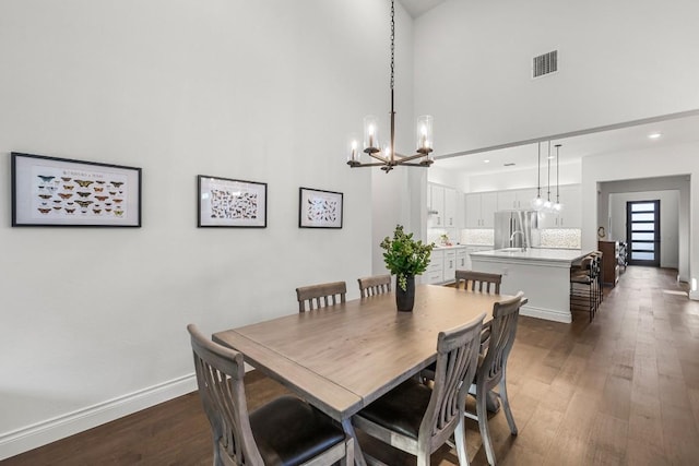 dining space with a chandelier, a towering ceiling, and dark wood-type flooring