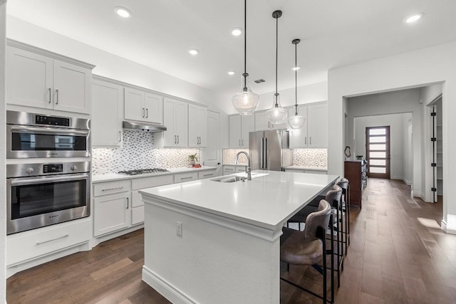 kitchen with sink, dark wood-type flooring, stainless steel appliances, pendant lighting, and a center island with sink