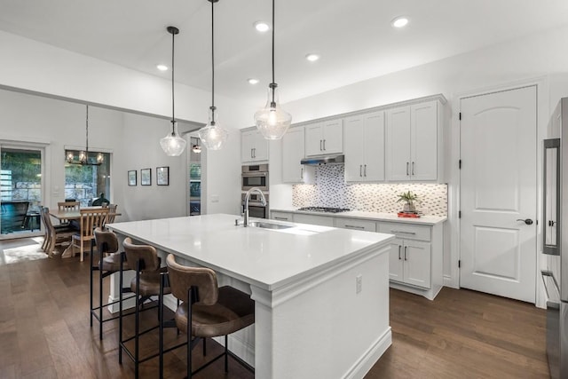 kitchen featuring decorative light fixtures, white cabinetry, dark wood-type flooring, and an island with sink