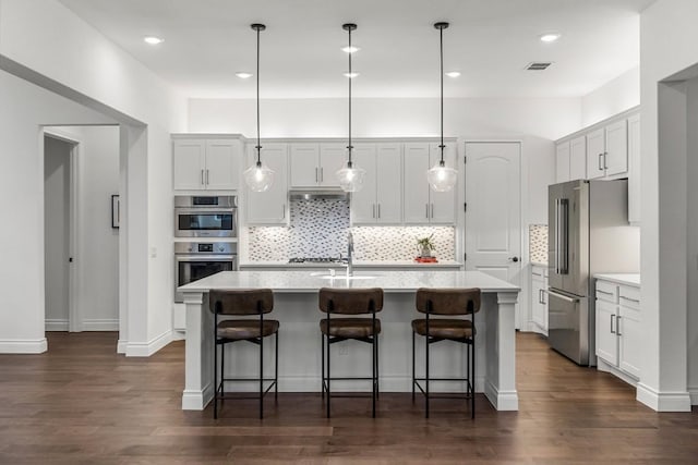 kitchen featuring white cabinetry, dark hardwood / wood-style floors, pendant lighting, a kitchen island with sink, and appliances with stainless steel finishes