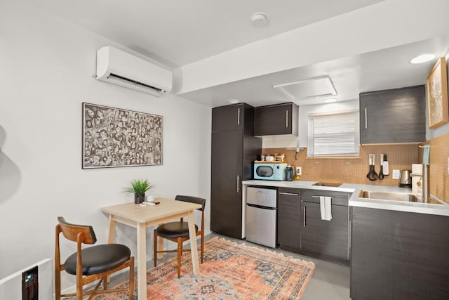 kitchen with decorative backsplash, dark brown cabinets, a wall mounted AC, sink, and stainless steel refrigerator