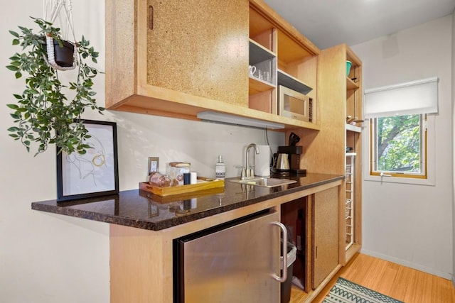 kitchen with dark stone countertops, sink, light hardwood / wood-style floors, and wine cooler