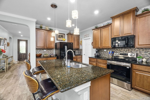 kitchen featuring brown cabinets, a center island with sink, a sink, dark stone countertops, and black appliances