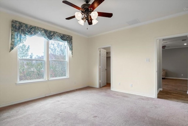 unfurnished bedroom featuring carpet floors, baseboards, ornamental molding, and a walk in closet