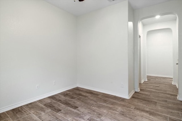 unfurnished room with dark wood-style floors, baseboards, arched walkways, and a ceiling fan