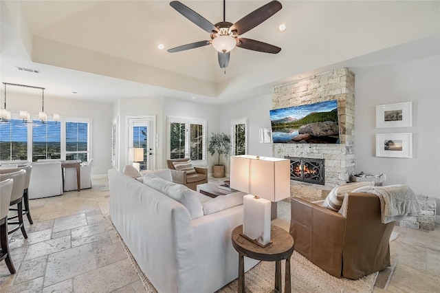 living room with ceiling fan with notable chandelier, a raised ceiling, and a fireplace