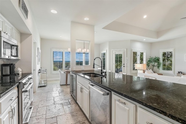 kitchen with sink, dark stone countertops, white cabinetry, stainless steel appliances, and a chandelier