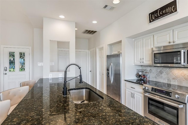 kitchen with backsplash, dark stone counters, stainless steel appliances, sink, and white cabinetry