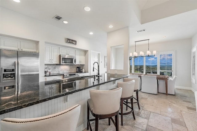 kitchen featuring a kitchen bar, appliances with stainless steel finishes, sink, white cabinets, and hanging light fixtures