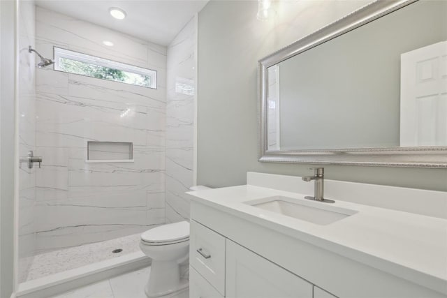 bathroom with a tile shower, vanity, and toilet