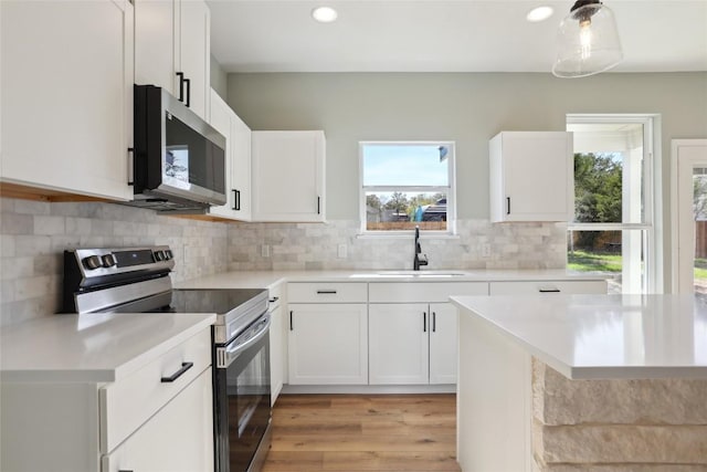 kitchen with decorative backsplash, appliances with stainless steel finishes, sink, white cabinets, and light hardwood / wood-style floors