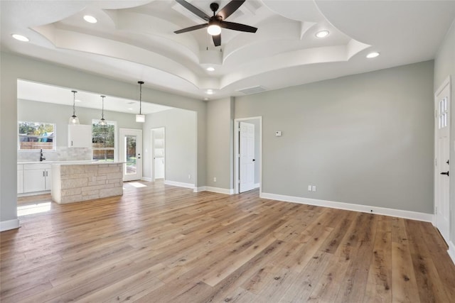 109 Creekside Dr, Bastrop, TX 78602 - unfurnished living room with recessed lighting, light wood-style floors, a ceiling fan, a raised ceiling, and a sink
