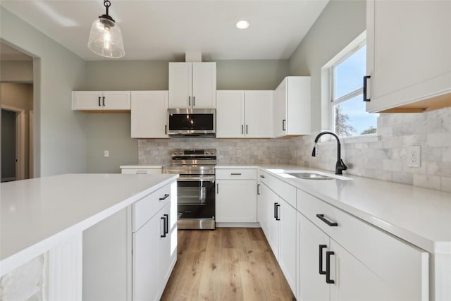 kitchen with sink, white cabinets, stainless steel appliances, and decorative light fixtures