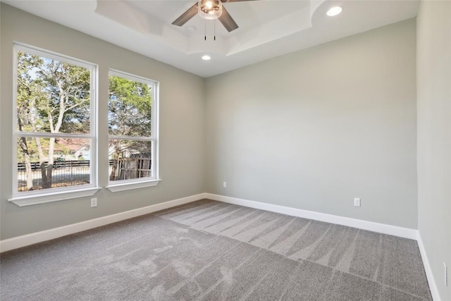 carpeted empty room featuring ceiling fan and a raised ceiling