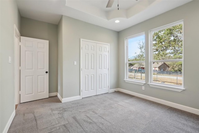 unfurnished bedroom featuring ceiling fan, light colored carpet, a tray ceiling, and a closet