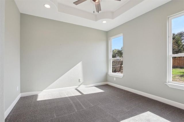 carpeted empty room with plenty of natural light, ceiling fan, and a tray ceiling