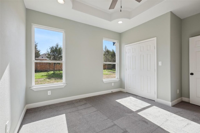 unfurnished bedroom with carpet floors, a closet, a raised ceiling, and ceiling fan