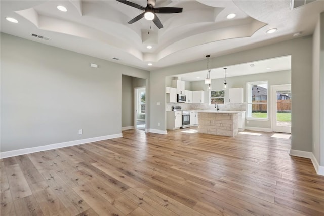 unfurnished living room with light wood-type flooring, a tray ceiling, ceiling fan, and sink