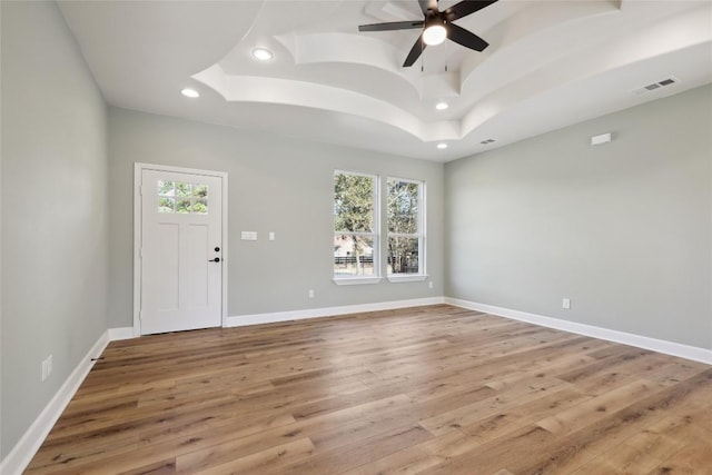 interior space featuring a raised ceiling, ceiling fan, and light hardwood / wood-style flooring