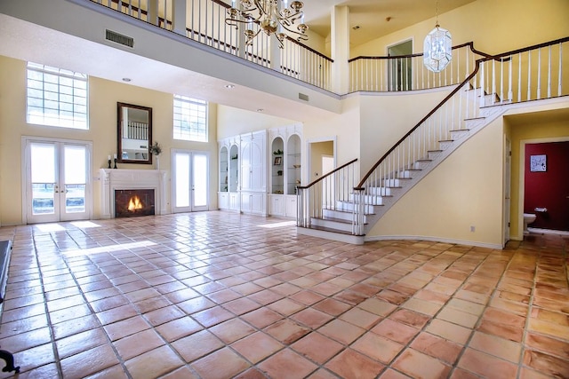 tiled foyer entrance featuring french doors, a towering ceiling, an inviting chandelier, and plenty of natural light