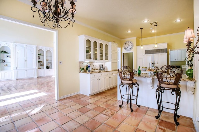 kitchen with light stone counters, ornamental molding, paneled fridge, white cabinetry, and a breakfast bar area