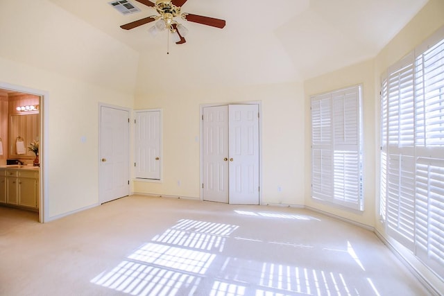 unfurnished bedroom featuring ceiling fan, ensuite bathroom, vaulted ceiling, light carpet, and two closets