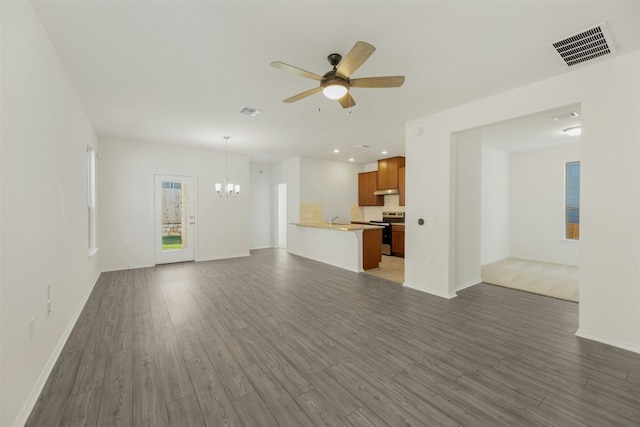 unfurnished living room featuring ceiling fan with notable chandelier and dark hardwood / wood-style floors