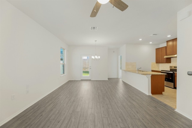 unfurnished living room featuring ceiling fan with notable chandelier, light wood-type flooring, and sink