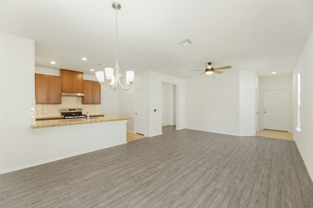 12521 Orchard Grove Ln, Manor, TX 78653 - kitchen featuring stainless steel electric range oven, brown cabinets, under cabinet range hood, backsplash, and light wood-style flooring