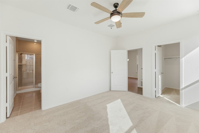 unfurnished bedroom with a walk in closet, ensuite bathroom, ceiling fan, and light colored carpet