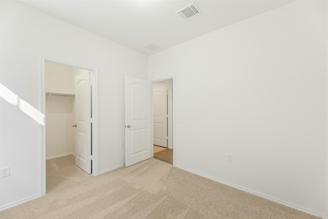 unfurnished bedroom with light colored carpet, a walk in closet, and a closet