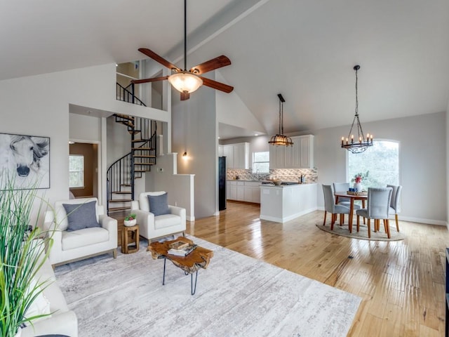 living room with ceiling fan with notable chandelier, light wood-type flooring, and high vaulted ceiling