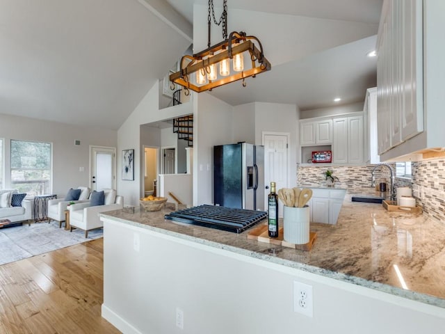 kitchen with kitchen peninsula, light wood-type flooring, pendant lighting, white cabinets, and stainless steel fridge with ice dispenser