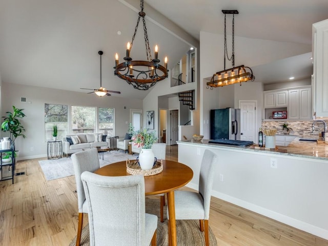 dining area with light wood-type flooring, ceiling fan with notable chandelier, sink, beam ceiling, and high vaulted ceiling