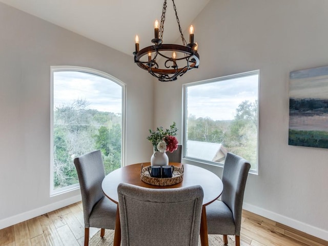 dining area with light wood-type flooring, vaulted ceiling, a healthy amount of sunlight, and a notable chandelier